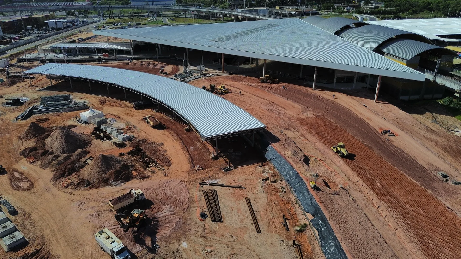 Vista aérea de terminal em estrutura metálica com cobertura curva, obra em fase avançada
